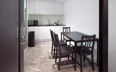 office kitchen with a table, six chairs, a fridge, microwave, sink, bin and cupboards